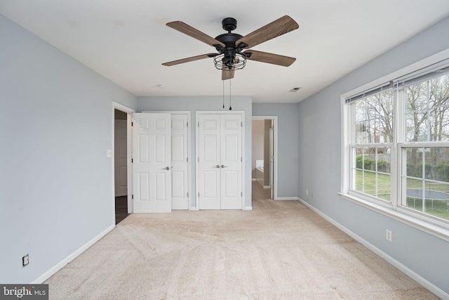 unfurnished bedroom with baseboards, two closets, carpet flooring, and a ceiling fan