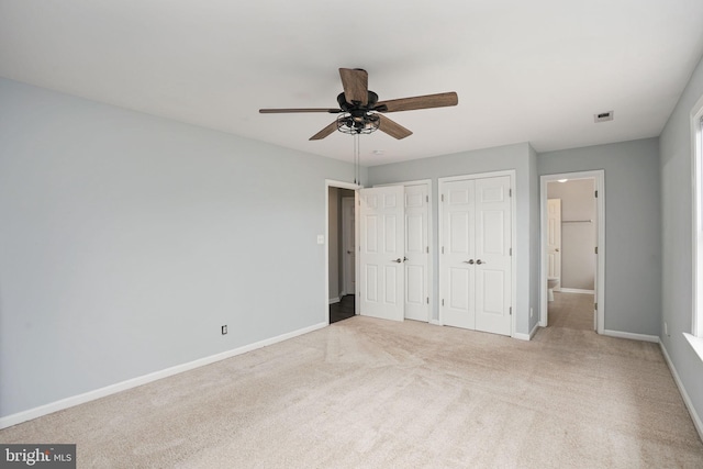 unfurnished bedroom featuring carpet flooring, a ceiling fan, baseboards, visible vents, and two closets
