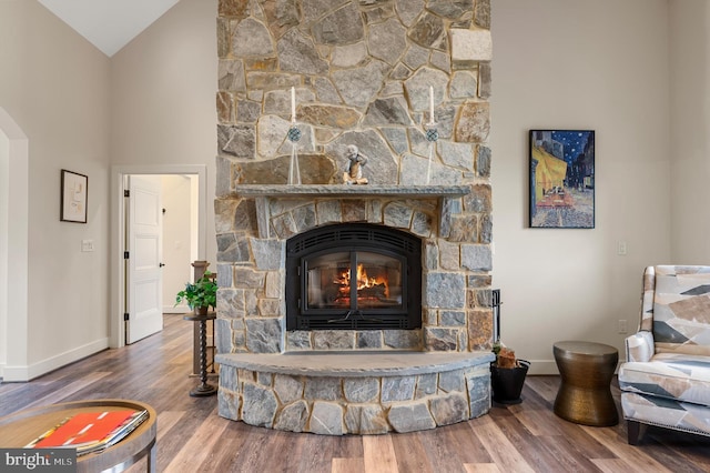 living room featuring baseboards, wood finished floors, a stone fireplace, and high vaulted ceiling