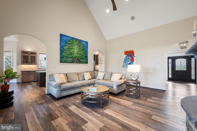 living room featuring high vaulted ceiling, arched walkways, baseboards, dark wood-style flooring, and recessed lighting