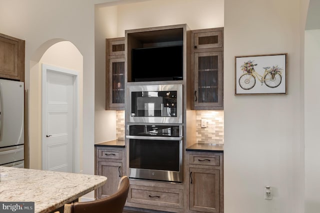kitchen with stainless steel oven, glass insert cabinets, tasteful backsplash, and freestanding refrigerator