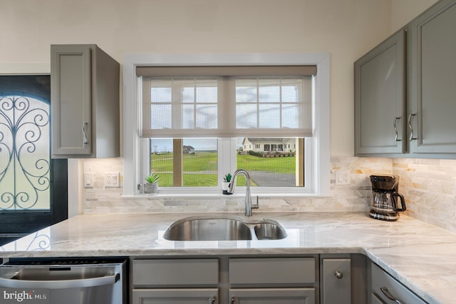 kitchen with decorative backsplash, stainless steel dishwasher, a sink, and gray cabinets