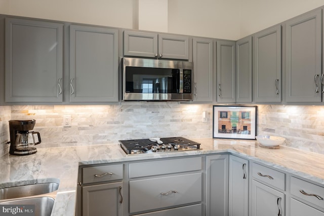 kitchen featuring decorative backsplash, appliances with stainless steel finishes, gray cabinetry, and light stone counters
