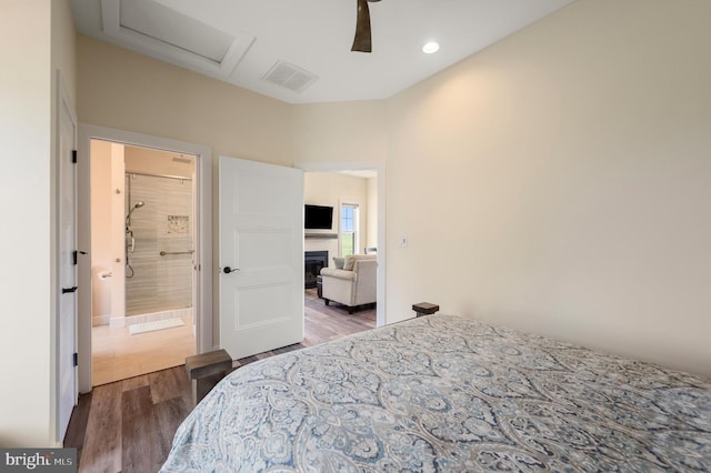 bedroom featuring attic access, a glass covered fireplace, wood finished floors, and visible vents