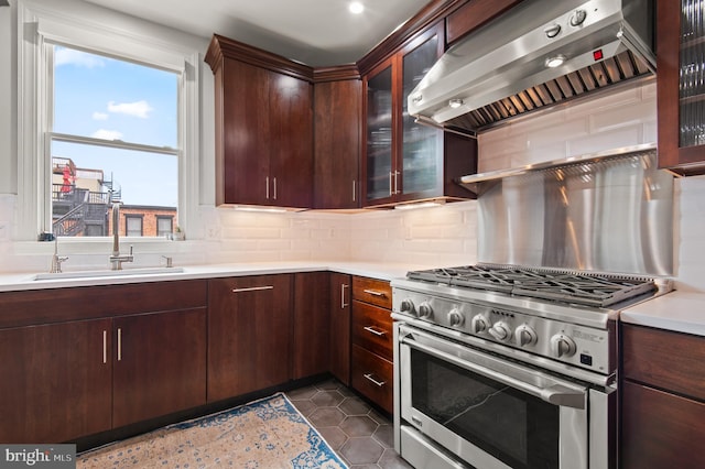 kitchen featuring light countertops, stainless steel range, backsplash, a sink, and wall chimney exhaust hood