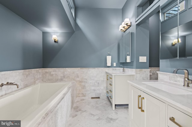 bathroom with a bath, a sink, tile walls, and two vanities