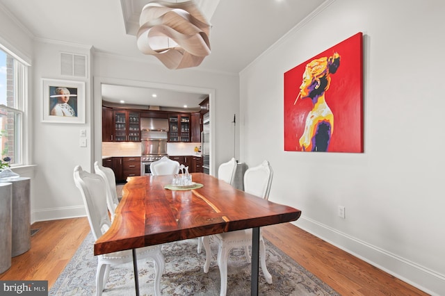 dining space featuring baseboards, light wood-style flooring, visible vents, and crown molding