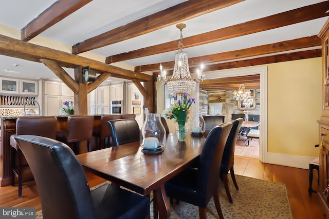 dining room with beam ceiling, baseboards, light wood-style floors, and a chandelier