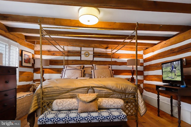 bedroom featuring beamed ceiling, wooden walls, and wood finished floors