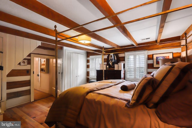 bedroom with beamed ceiling, wooden walls, visible vents, and hardwood / wood-style flooring