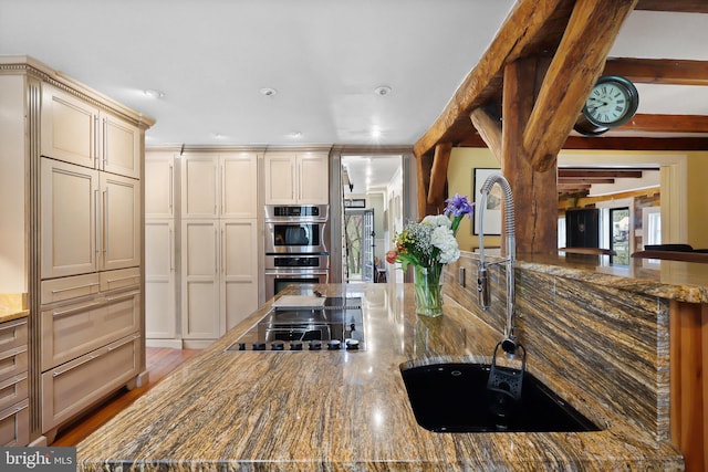 kitchen with dark stone counters, a sink, stainless steel double oven, cream cabinets, and stovetop
