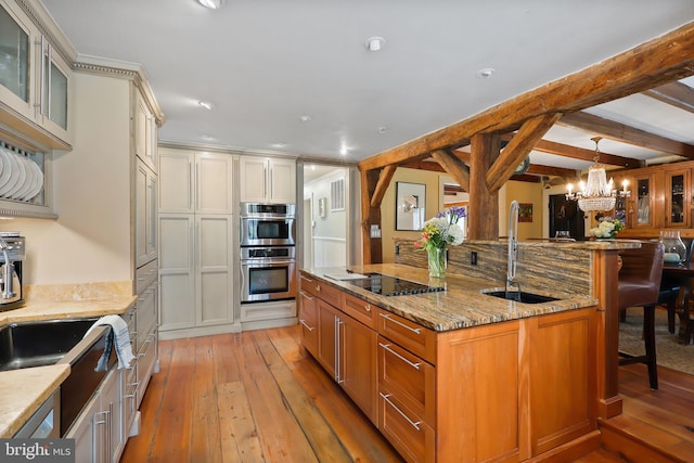 kitchen with black electric cooktop, double oven, light wood finished floors, a sink, and a breakfast bar area