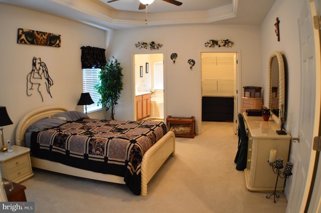 bedroom featuring ensuite bath, a tray ceiling, a ceiling fan, and light colored carpet