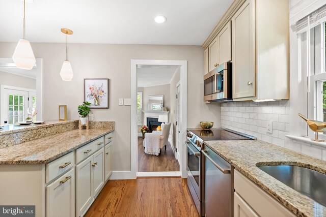 8620 Conover Pl, Alexandria, VA 22308 - kitchen with stainless steel appliances, light wood-type flooring, a peninsula, tasteful backsplash, and a warm lit fireplace