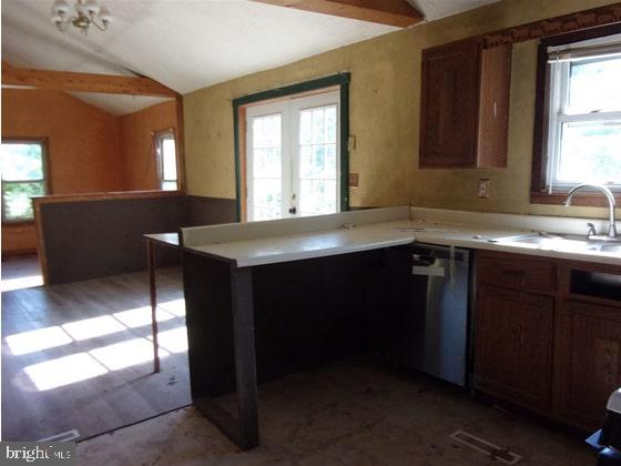 kitchen featuring a peninsula, light countertops, a sink, lofted ceiling, and dishwasher