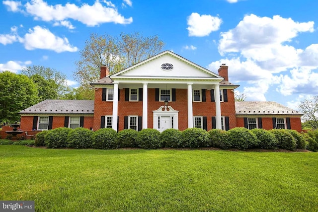 greek revival inspired property featuring a chimney, a front yard, and brick siding