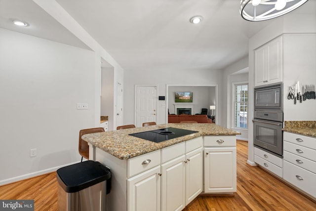 kitchen featuring a center island, oven, built in microwave, light wood-style floors, and black electric stovetop