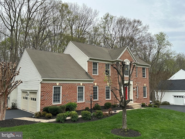 colonial home with a garage, roof with shingles, a front lawn, brick siding, and driveway
