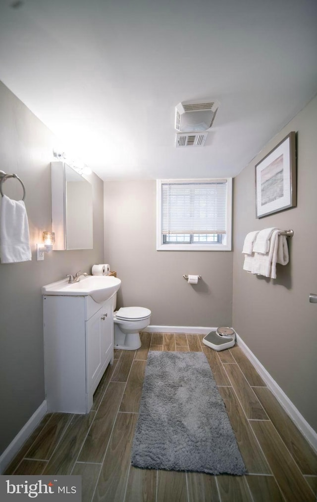 bathroom with toilet, baseboards, vanity, and wood finish floors