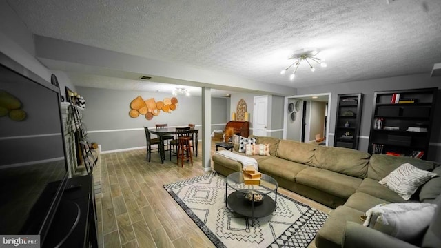 living area with a notable chandelier, a textured ceiling, baseboards, visible vents, and wood finished floors
