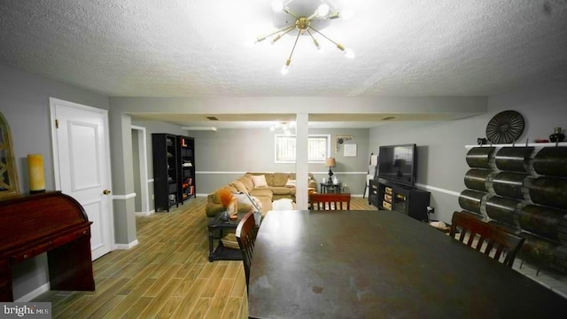living area featuring a textured ceiling, a chandelier, baseboards, and light wood-style floors