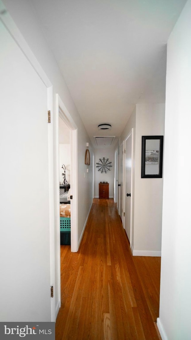 corridor featuring attic access, baseboards, and light wood-style floors