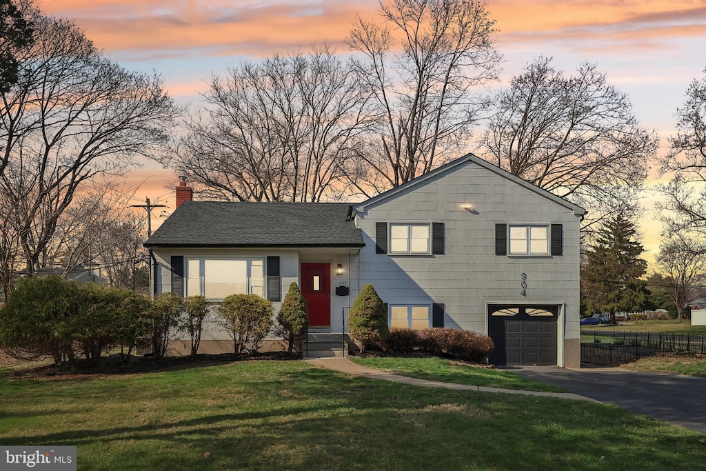 split level home with a chimney, fence, aphalt driveway, a garage, and a yard