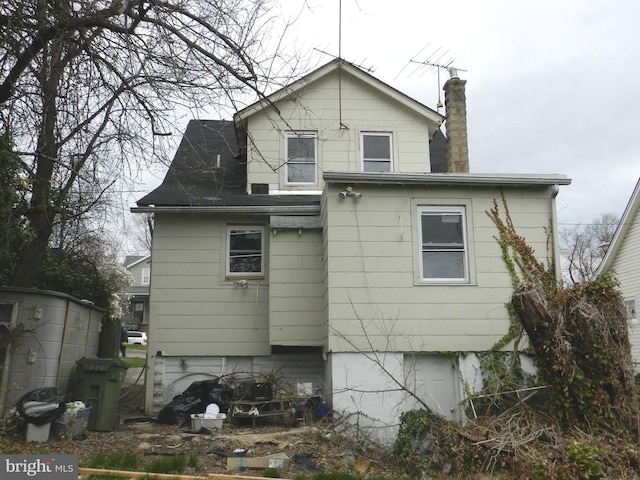 back of property featuring a chimney and roof with shingles