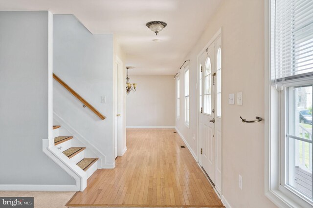 entryway featuring a wealth of natural light, a chandelier, light wood-style floors, and stairs