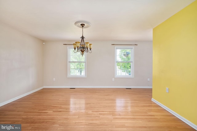 spare room with baseboards, light wood-type flooring, and a notable chandelier