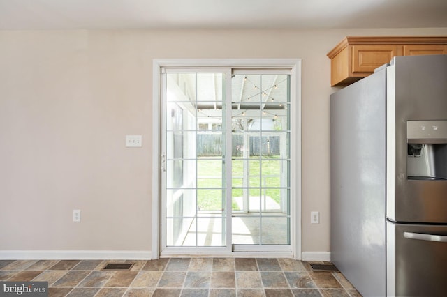kitchen featuring stainless steel fridge with ice dispenser, plenty of natural light, baseboards, and stone finish flooring