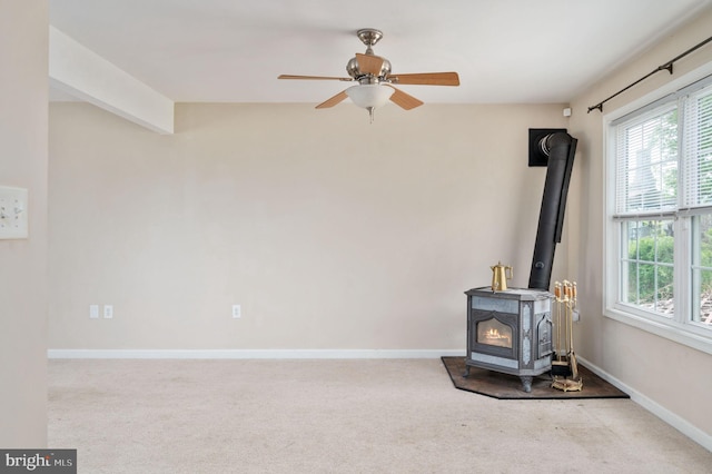unfurnished living room with a ceiling fan, a wood stove, carpet, and plenty of natural light