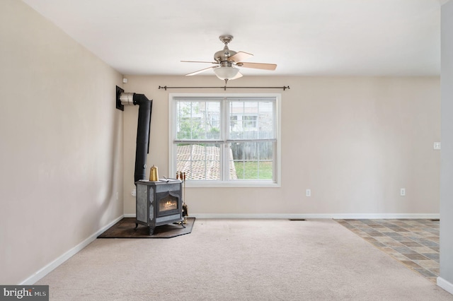 carpeted living room with a wood stove, baseboards, and a ceiling fan