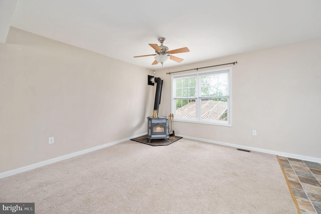 interior space with a wood stove, ceiling fan, carpet, visible vents, and baseboards