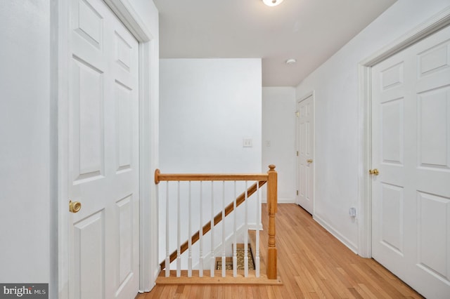 hall featuring an upstairs landing, light wood-style floors, and baseboards