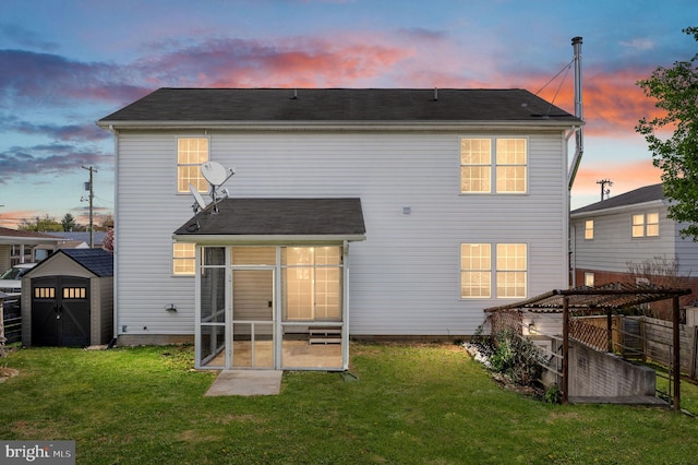 back of house at dusk with a storage unit, a sunroom, an outbuilding, and a lawn