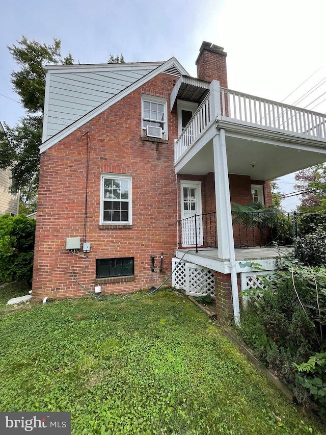 view of side of property featuring a yard, a chimney, cooling unit, a balcony, and brick siding