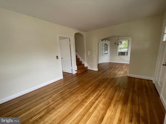 empty room with wood-type flooring, baseboards, stairway, and arched walkways