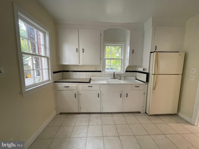 kitchen featuring freestanding refrigerator, baseboards, and white cabinetry