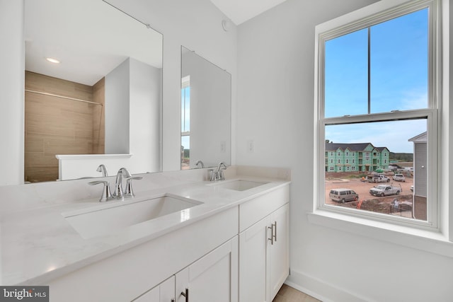 bathroom featuring double vanity, a tile shower, baseboards, and a sink