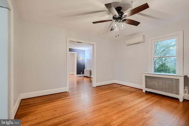 spare room with ceiling fan, a wall unit AC, radiator heating unit, and light wood-style flooring