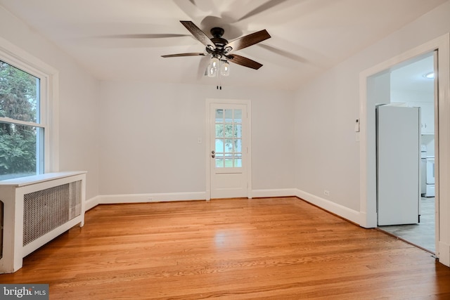 spare room featuring baseboards, light wood-style flooring, ceiling fan, and radiator heating unit