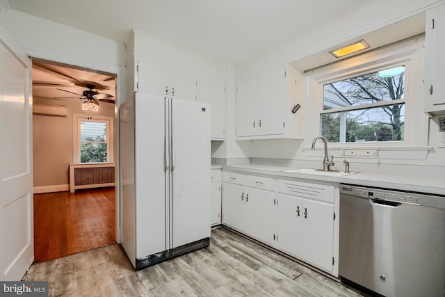 kitchen with a sink, radiator heating unit, light wood-style flooring, freestanding refrigerator, and stainless steel dishwasher