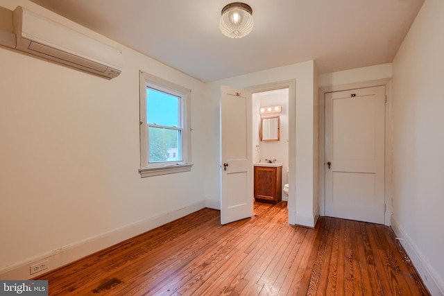 unfurnished bedroom featuring light wood-style floors, baseboards, and a wall mounted air conditioner