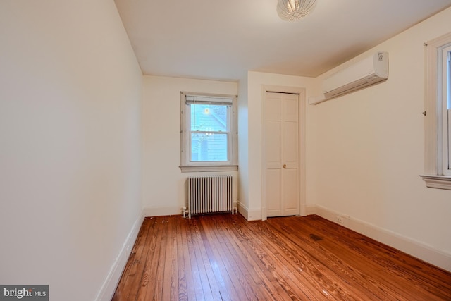 unfurnished room with an AC wall unit, baseboards, radiator heating unit, and hardwood / wood-style flooring