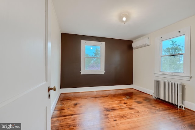 empty room with wood-type flooring, a wall mounted AC, a wealth of natural light, and radiator