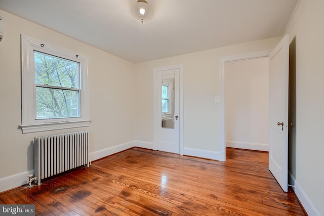 unfurnished room featuring radiator heating unit, baseboards, and wood finished floors