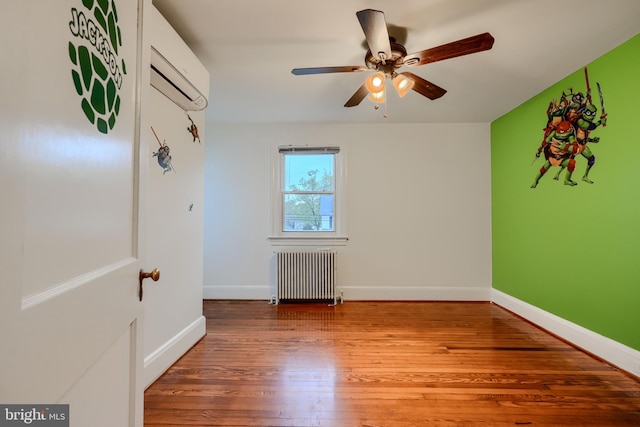 spare room with radiator, wood finished floors, baseboards, a wall mounted air conditioner, and ceiling fan