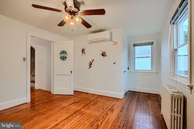 empty room with ceiling fan, arched walkways, an AC wall unit, light wood-style floors, and radiator