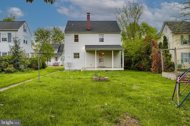 back of property featuring a yard, a chimney, covered porch, and roof with shingles